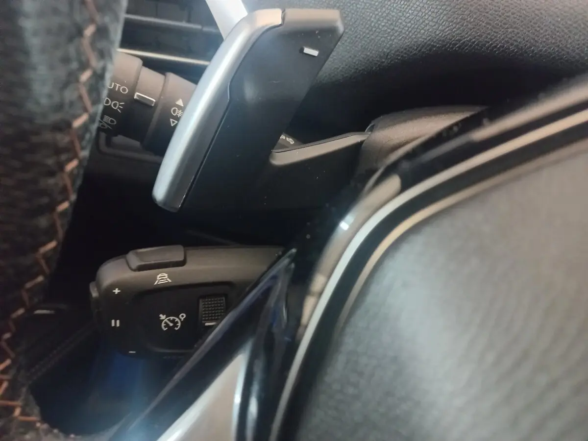 Gros plan sur la commande de régulateur de vitesse et palettes au volant du Peugeot 3008 gris clair, intérieur noir.