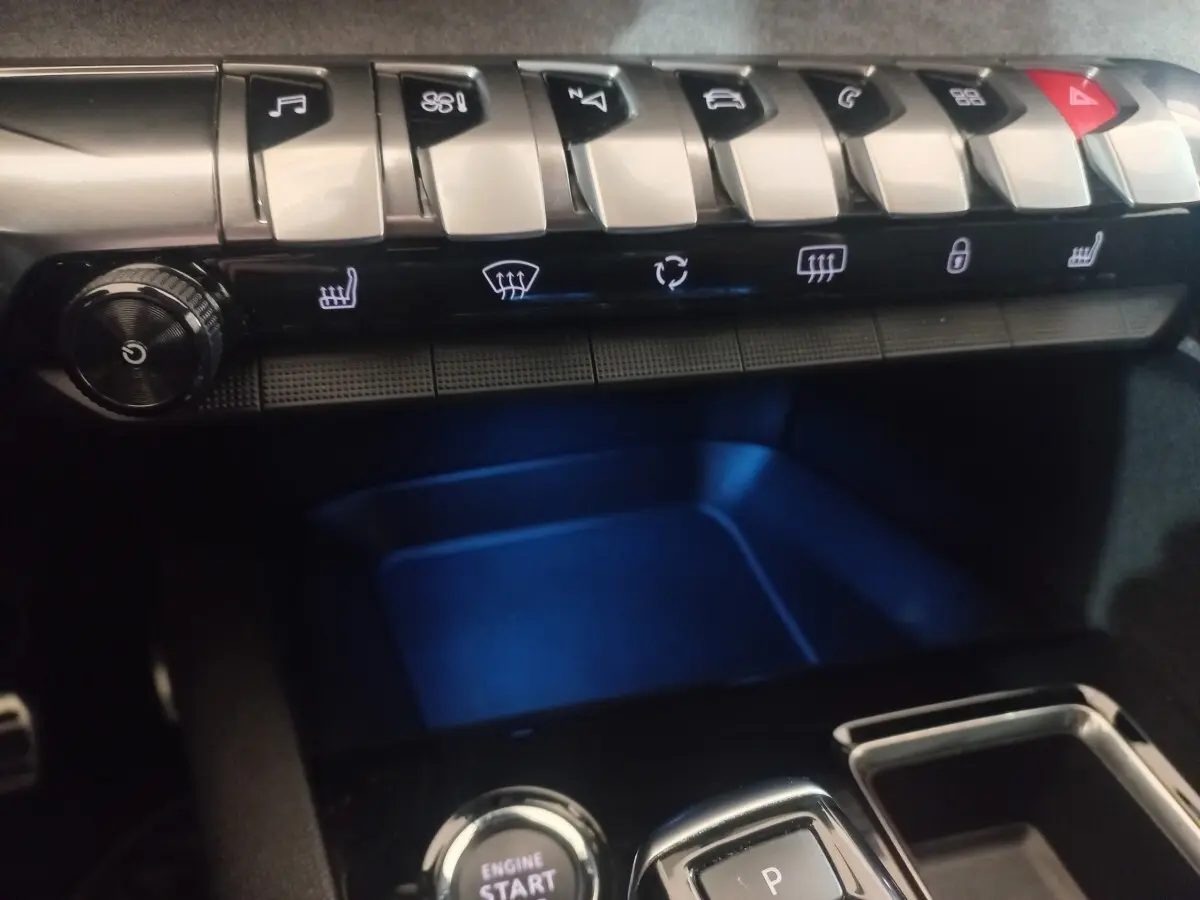 Gros plan sur la console centrale du Peugeot 3008 gris clair, avec boutons de contrôle et éclairage bleu intérieur.