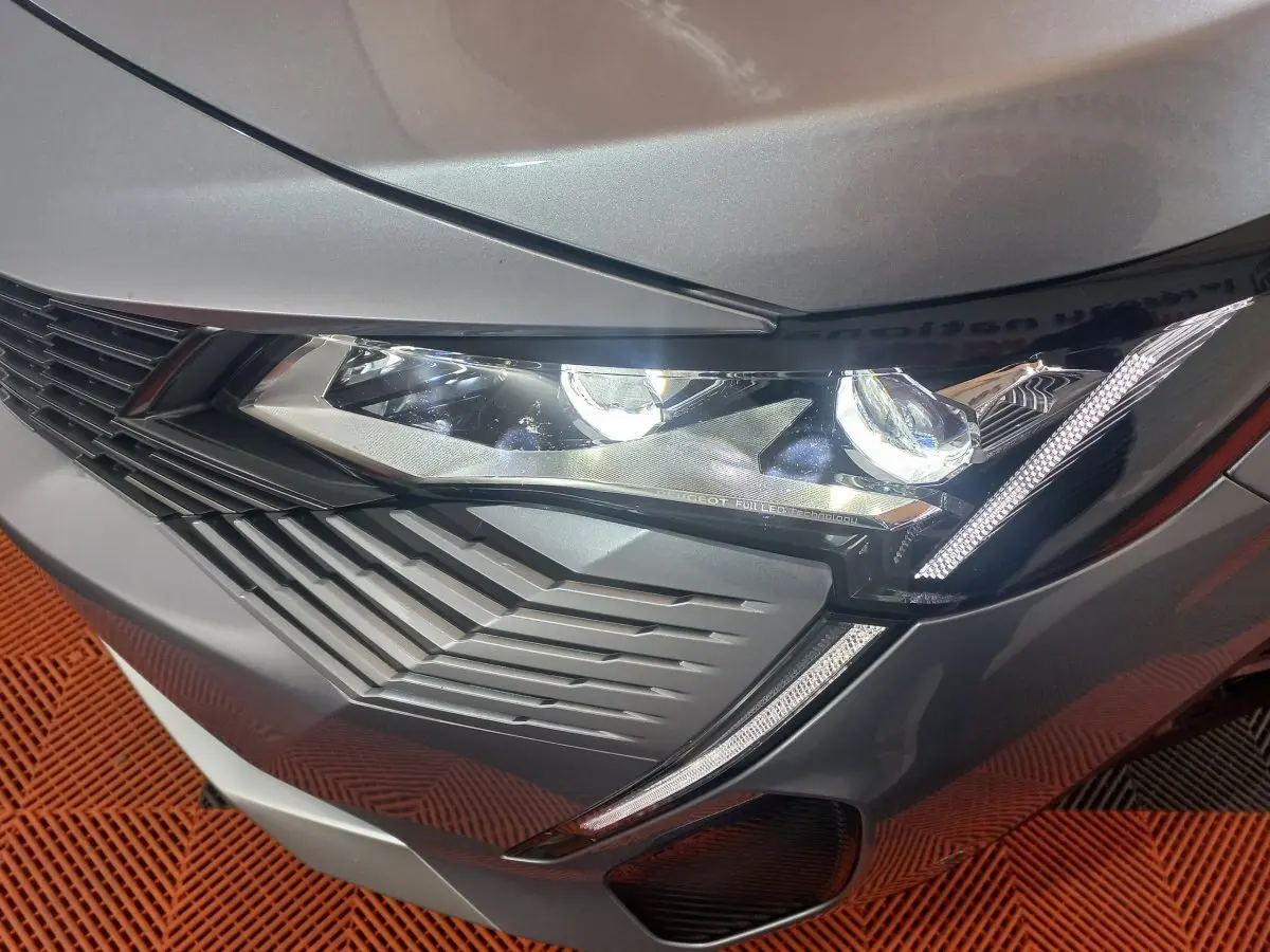 Gros plan sur le phare avant droit d’un Peugeot 3008 gris clair 2022 avec signature lumineuse LED distinctive.