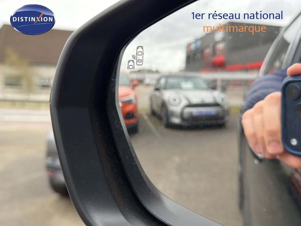 Rétroviseur côté droit d’un Citroën C5 Aircross noir métal 2025, avec reflet d’un parking et main tenant un smartphone.