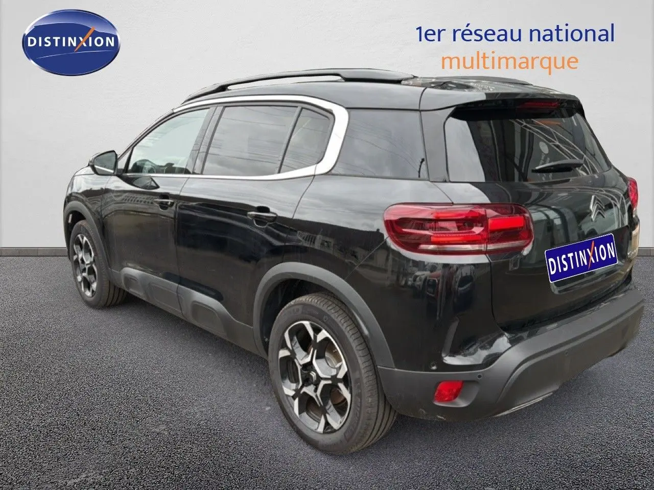 Vue 3/4 arrière droite d'un Citroën C5 Aircross noir métal avec jantes bi-ton et barres de toit visibles.