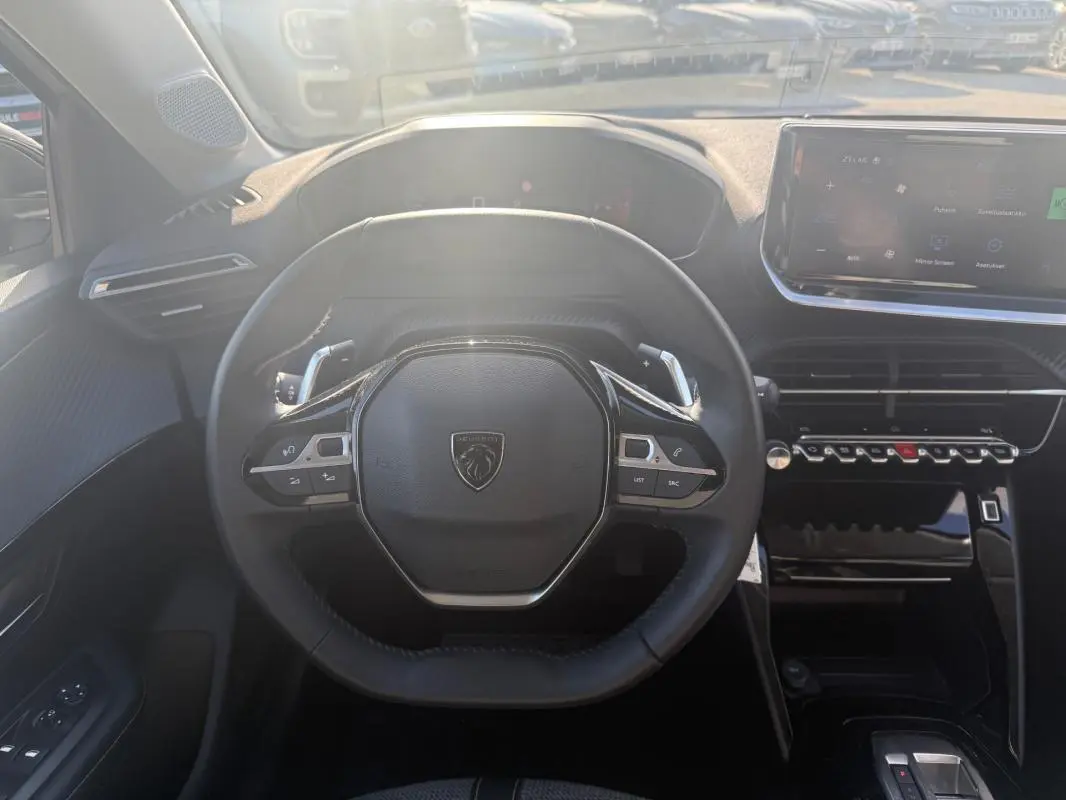 Vue intérieure centrée sur le volant compact de la Peugeot 208 Hybrid 110 e-DCS6 Allure avec tableau de bord numérique et écran tactile.