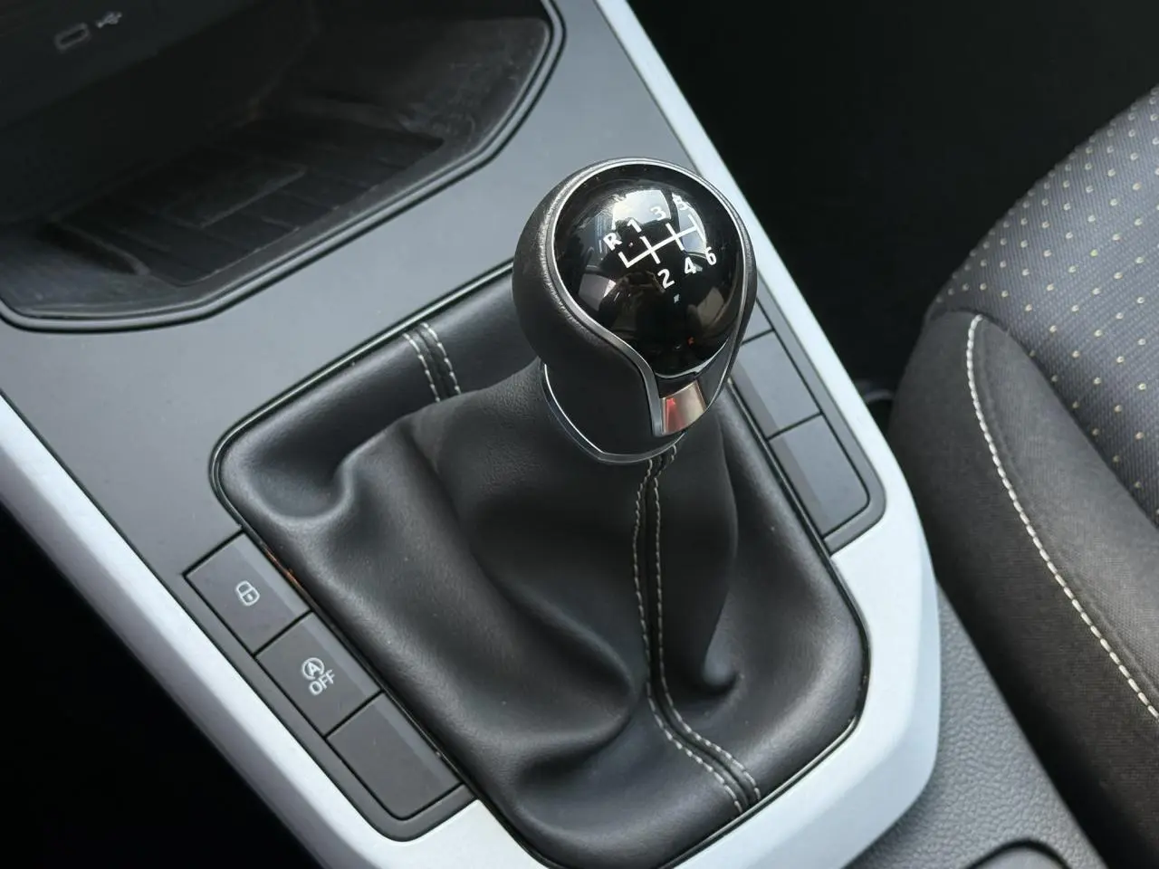 Gros plan sur le levier de vitesses manuel noir avec coutures blanches dans l’habitacle du SEAT Arona TSI 115 Style.