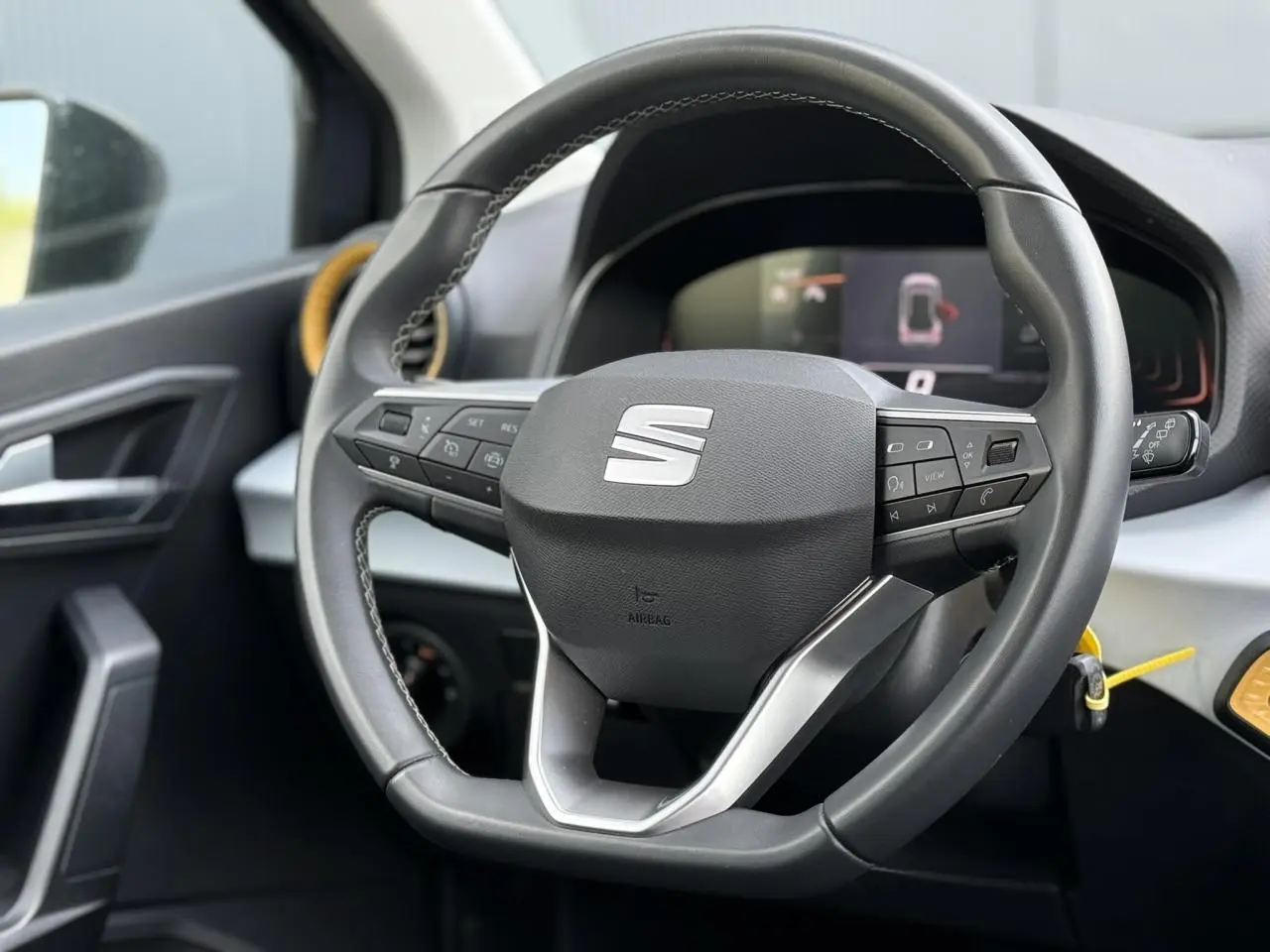 Vue rapprochée du volant multifonction noir du SEAT Arona 2025 avec détails argentés et tableau de bord digital en arrière-plan.