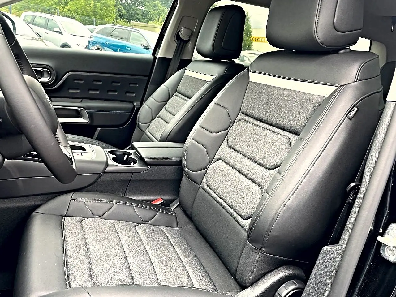 Vue intérieure côté conducteur du Citroën C5 Aircross 2025 noir, sièges tissu et cuir avec accoudoir central.