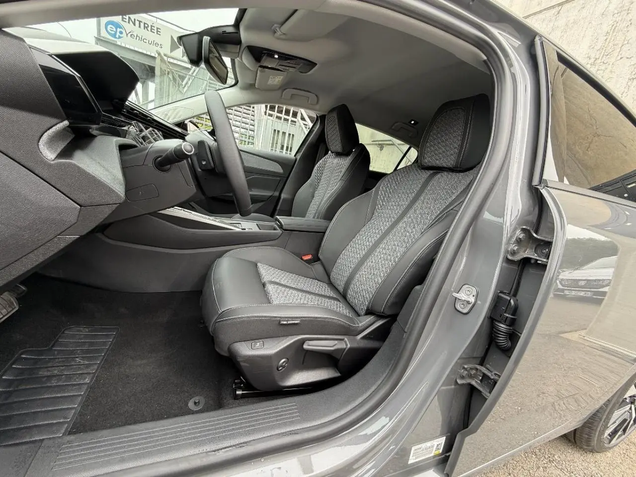 Intérieur côté conducteur du Peugeot 308 gris sélénite 2026, sièges tissu et cuir avec surpiqûres contrastées visibles.