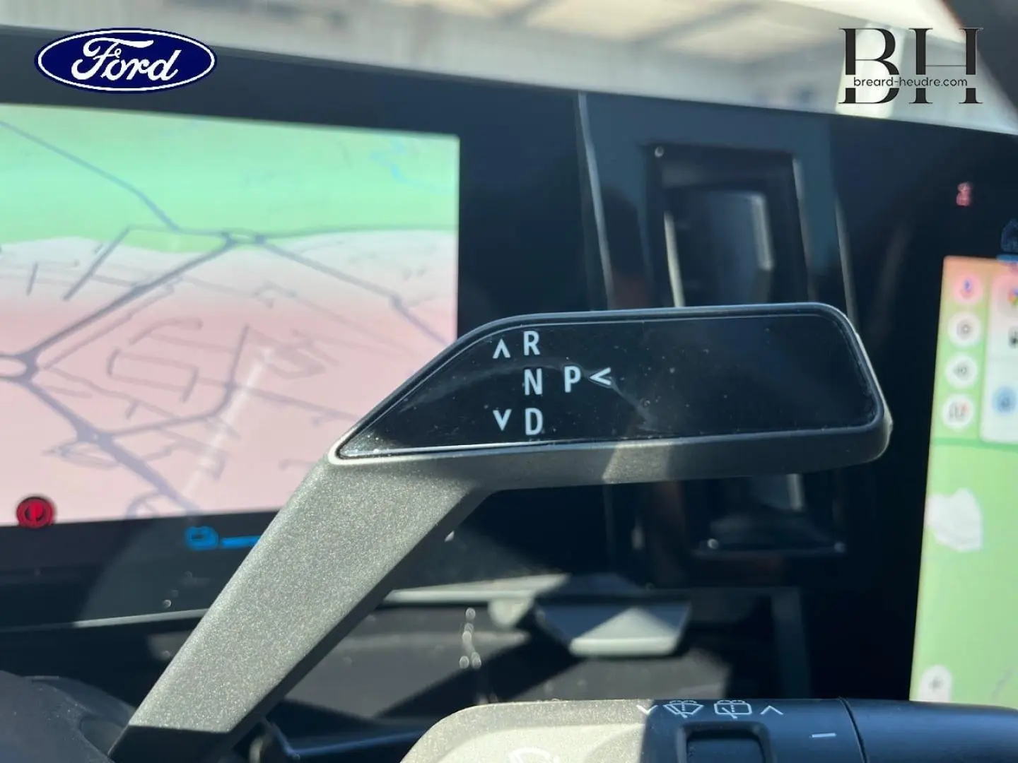 Le véhicule Renault Austral bleu Iron est vu de l'intérieur, avec un focus sur le levier de vitesses automatique et l'écran tactile GPS.
