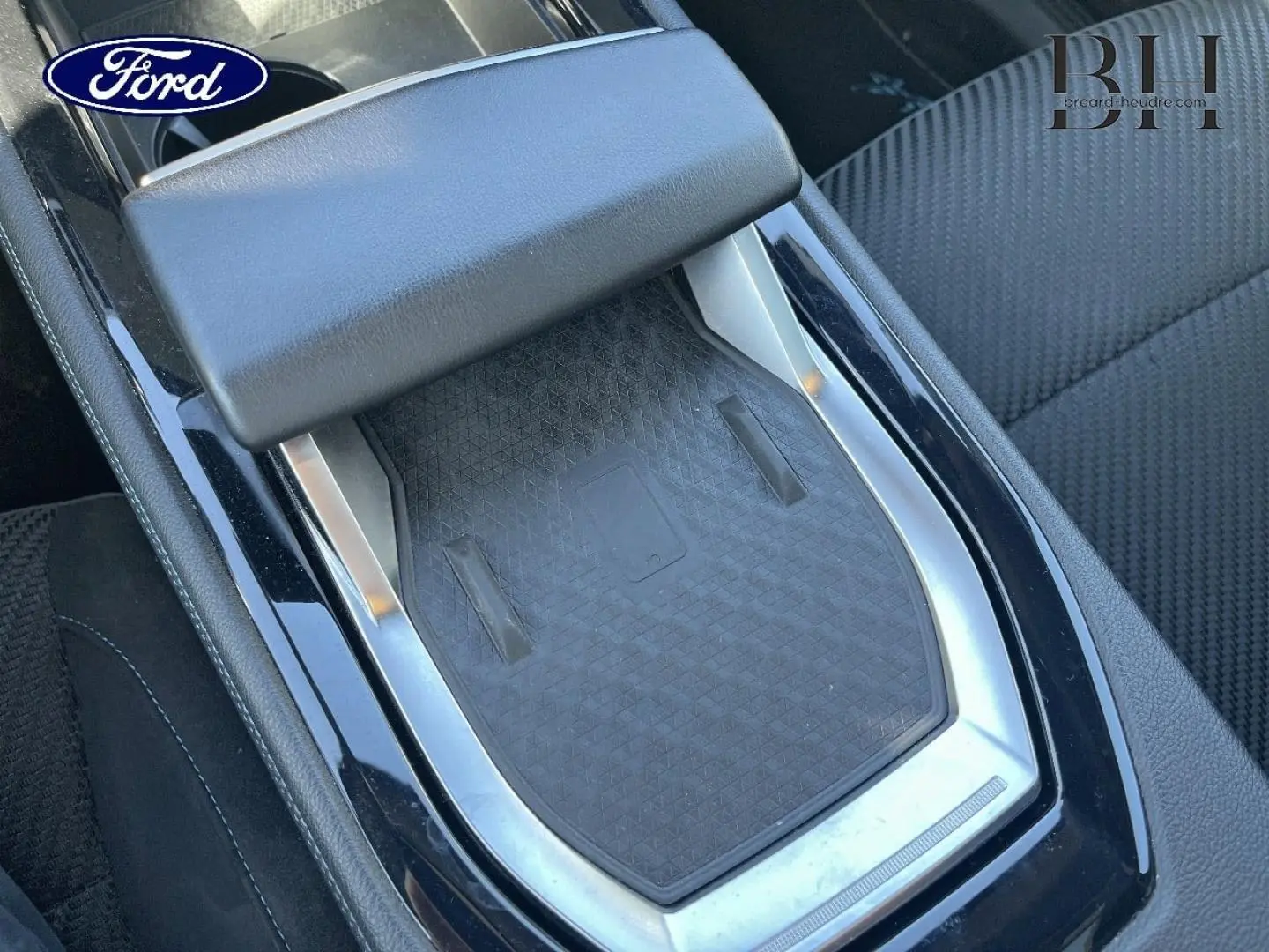 Gros plan sur la console centrale noire avec accoudoir et surface de recharge, intérieur tissu carbone/Alcantara bleu.