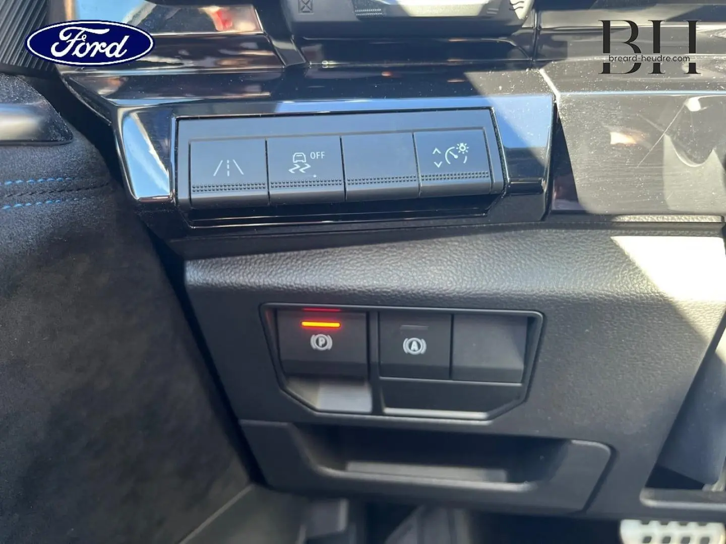 Panneau de commandes au tableau de bord avec boutons d'aide à la conduite et frein de parking électrique activé.