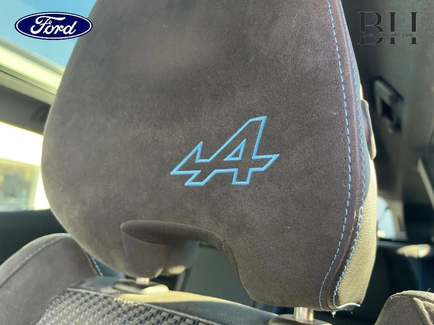 Gros plan sur l'appui-tête avant en alcantara noir avec logo Alpine bleu et surpiqûres bleues du Renault Austral Bleu Iron.