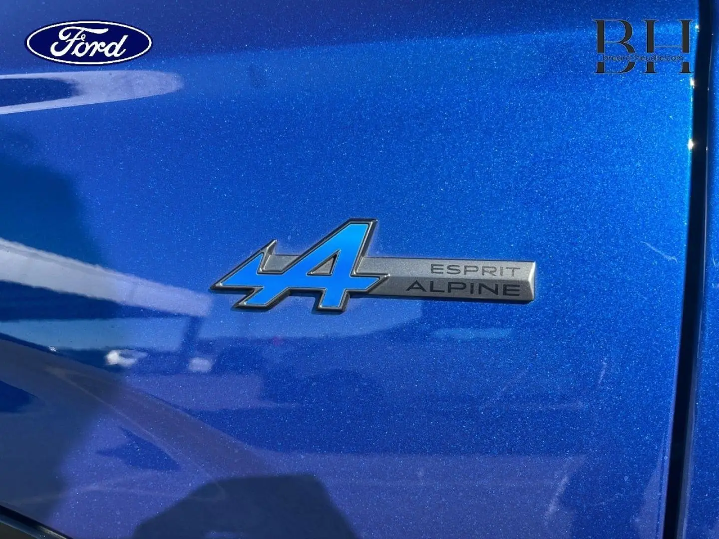 Gros plan sur l'emblème Esprit Alpine bleu sur la carrosserie Bleu Iron d'une Renault Austral 2023.