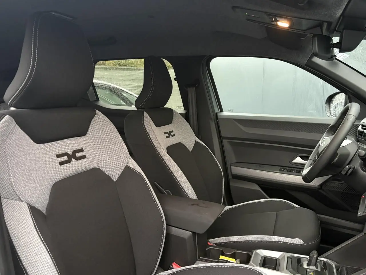 Vue intérieure côté droit du Dacia Duster 2026, sièges bi-ton gris clair et noir avec logo brodé sur appuie-tête.