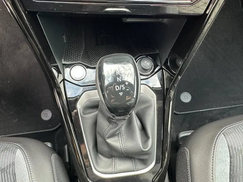 Le levier de vitesse automatique noir du Volkswagen T-Roc 1.5 TSI R-Line Edition 2025 vu de dessus, entouré de sièges gris.