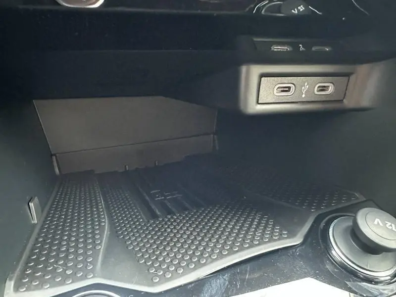 Gros plan sur la console centrale du Volkswagen T-Roc gris 2025, montrant les ports USB et un espace de rangement avec tapis antidérapant.