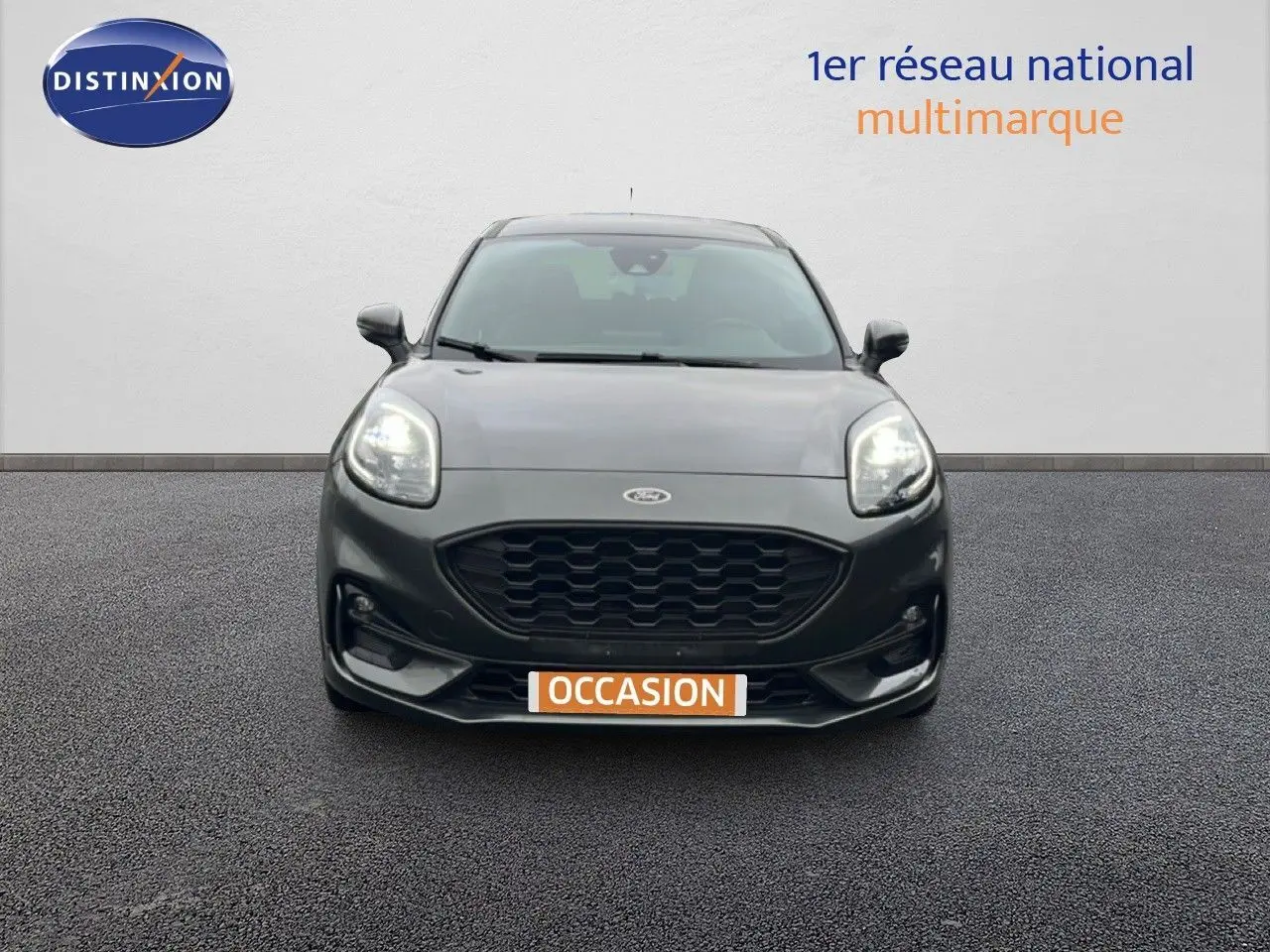 Vue frontale d'un Ford Puma gris magnétique 2024 avec calandre noire et phares allumés sur fond neutre.