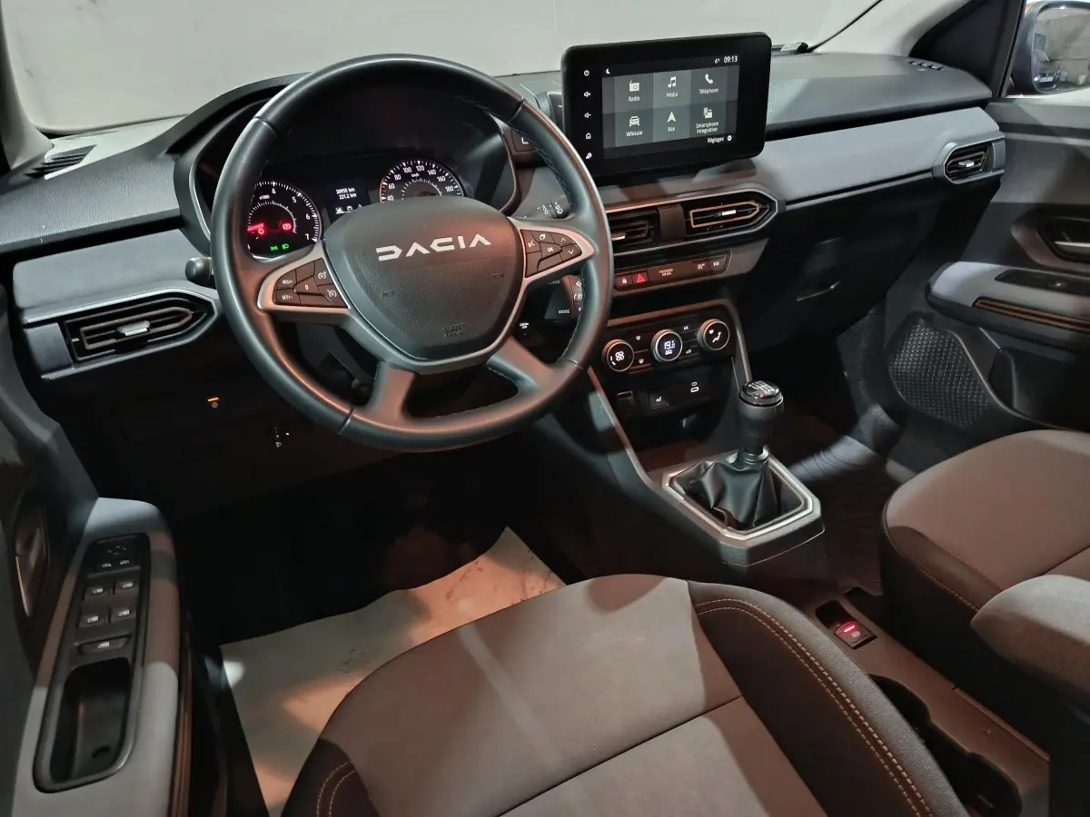 Vue intérieure avant de la Dacia Sandero 2024, volant multifonctions, écran tactile central et boîte manuelle visible.