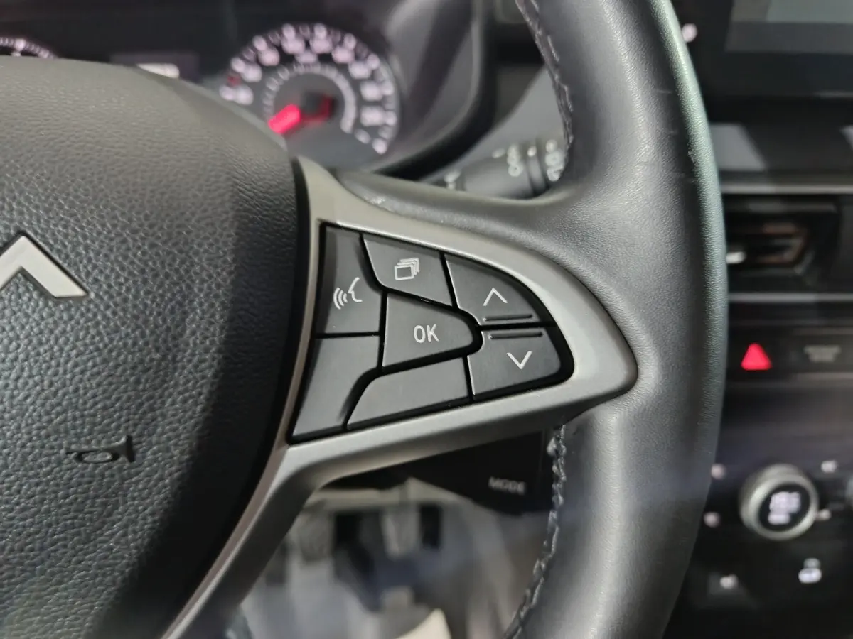 Gros plan sur le volant cuir noir de la Dacia Sandero 2024, avec commandes multifonctions visibles côté droit.