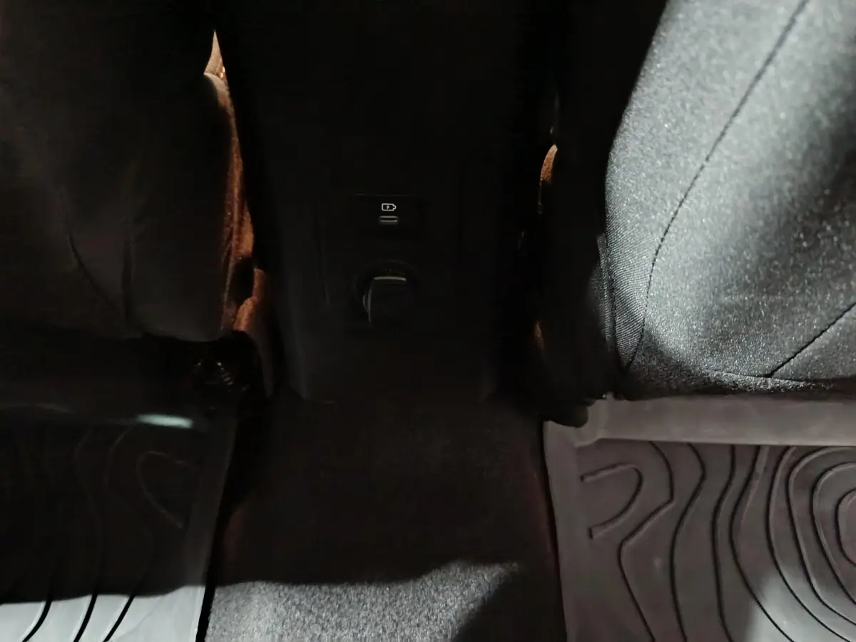 Vue intérieure centrée sur la console arrière noire avec prises USB et 12V entre les sièges avant du Dacia Sandero 2024.