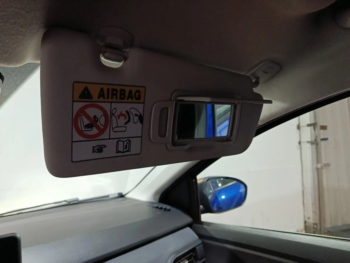 Vue intérieure côté passager du pare-soleil avec miroir et avertissement airbag, reflet bleu de la Dacia Sandero Extreme+ 2024.