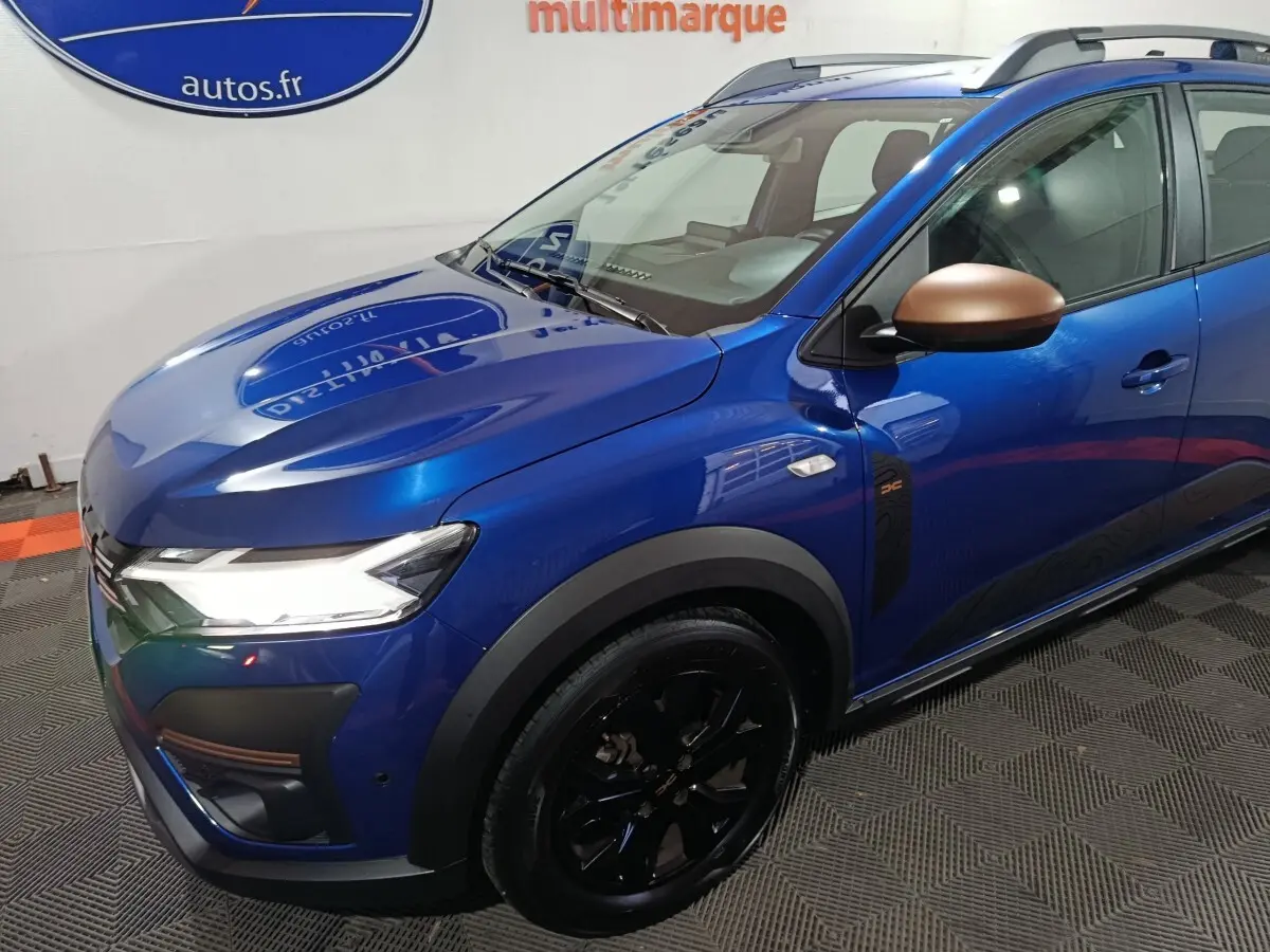 Vue 3/4 avant droit d'une Dacia Sandero Extreme+ TCe 110 bleu avec rétroviseurs bronze et jantes noires.