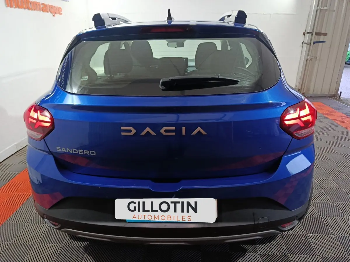 Vue arrière d'une Dacia Sandero bleu vif 2024, feux LED allumés et logo DACIA bien visible.
