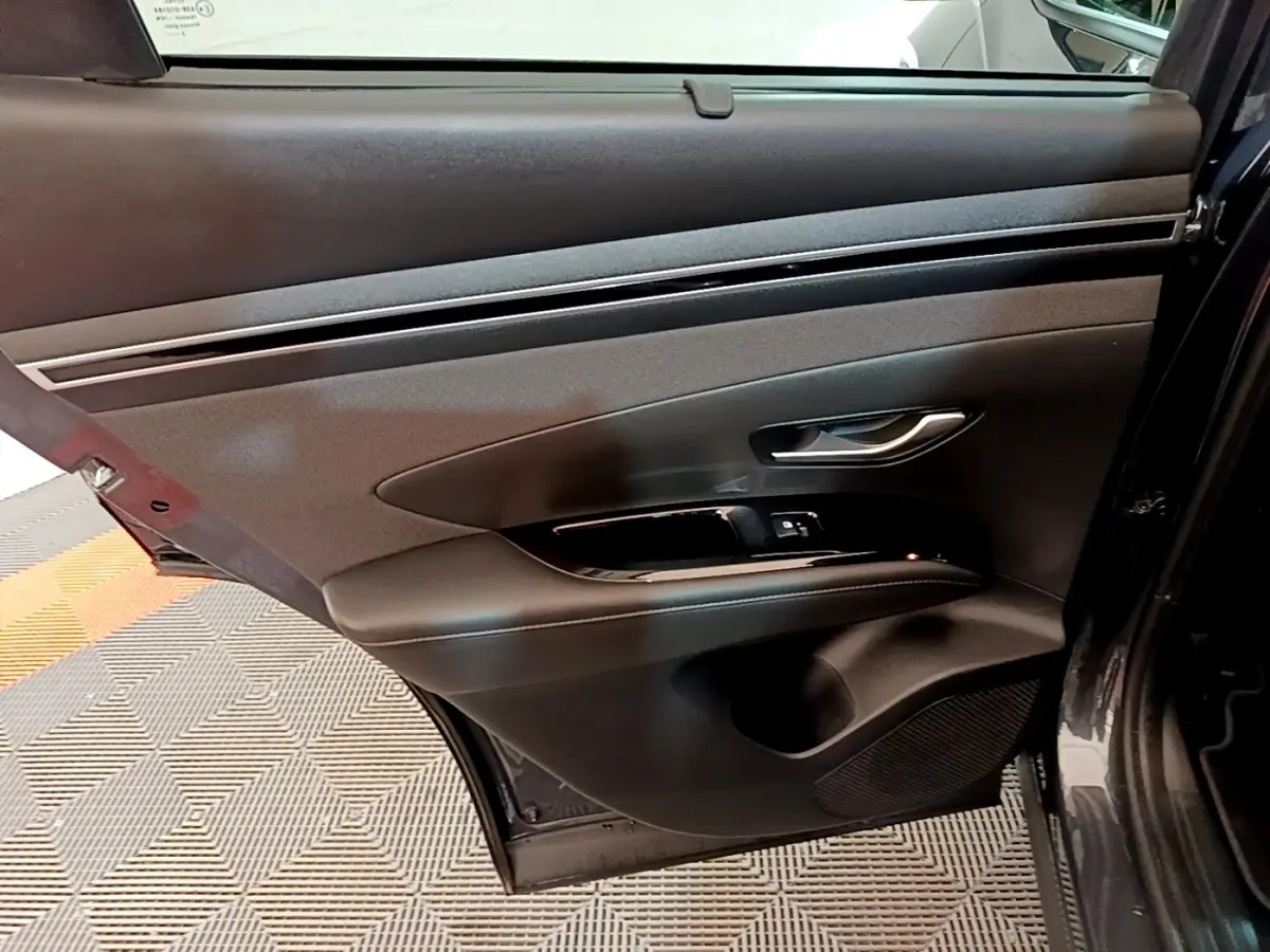 Vue intérieure de la porte arrière droite du Hyundai Tucson gris foncé, avec poignée argentée et commandes de fenêtre.