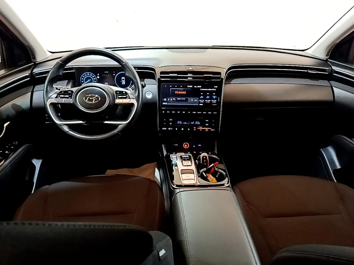 Vue intérieure avant du Hyundai Tucson 2022, tableau de bord noir avec écran tactile central et volant multifonctions.