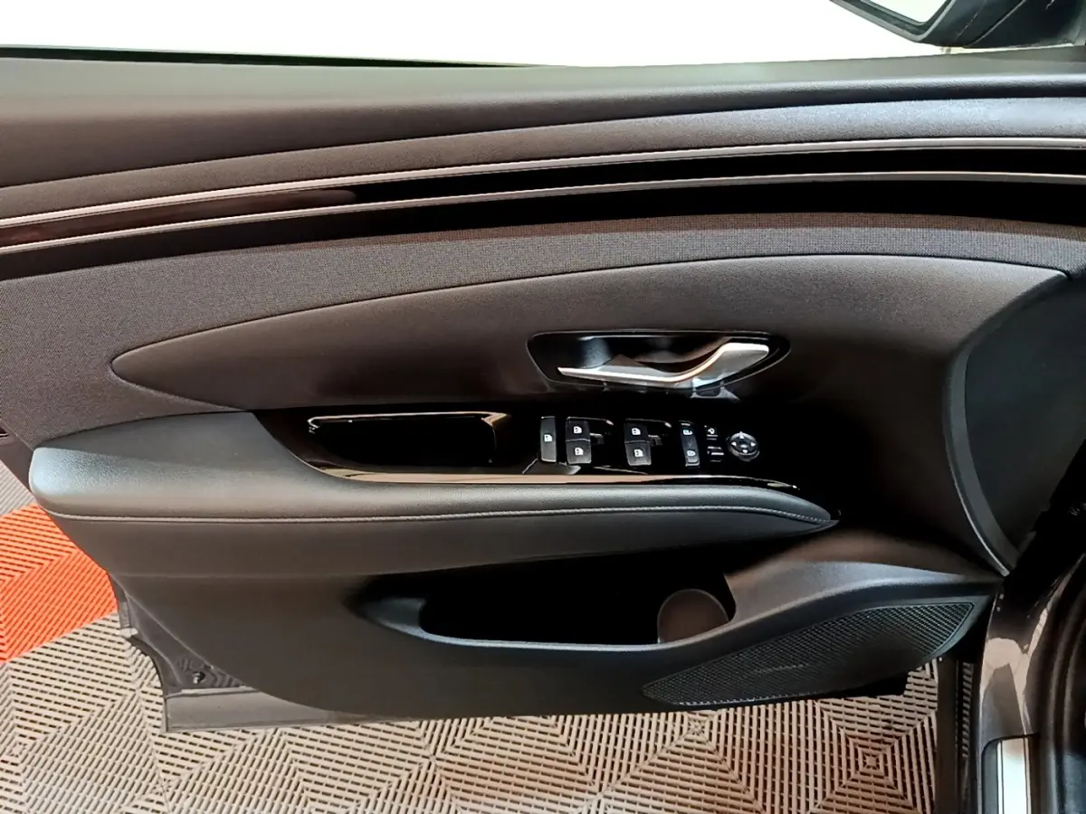 Vue latérale du panneau de porte avant gauche du Hyundai Tucson gris foncé avec commandes électriques et poignée argentée.