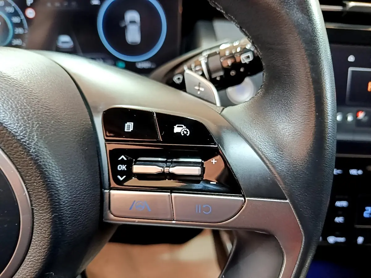 Gros plan sur les commandes du volant cuir noir du Hyundai Tucson 2022, avec boutons de régulateur de vitesse et assistance.