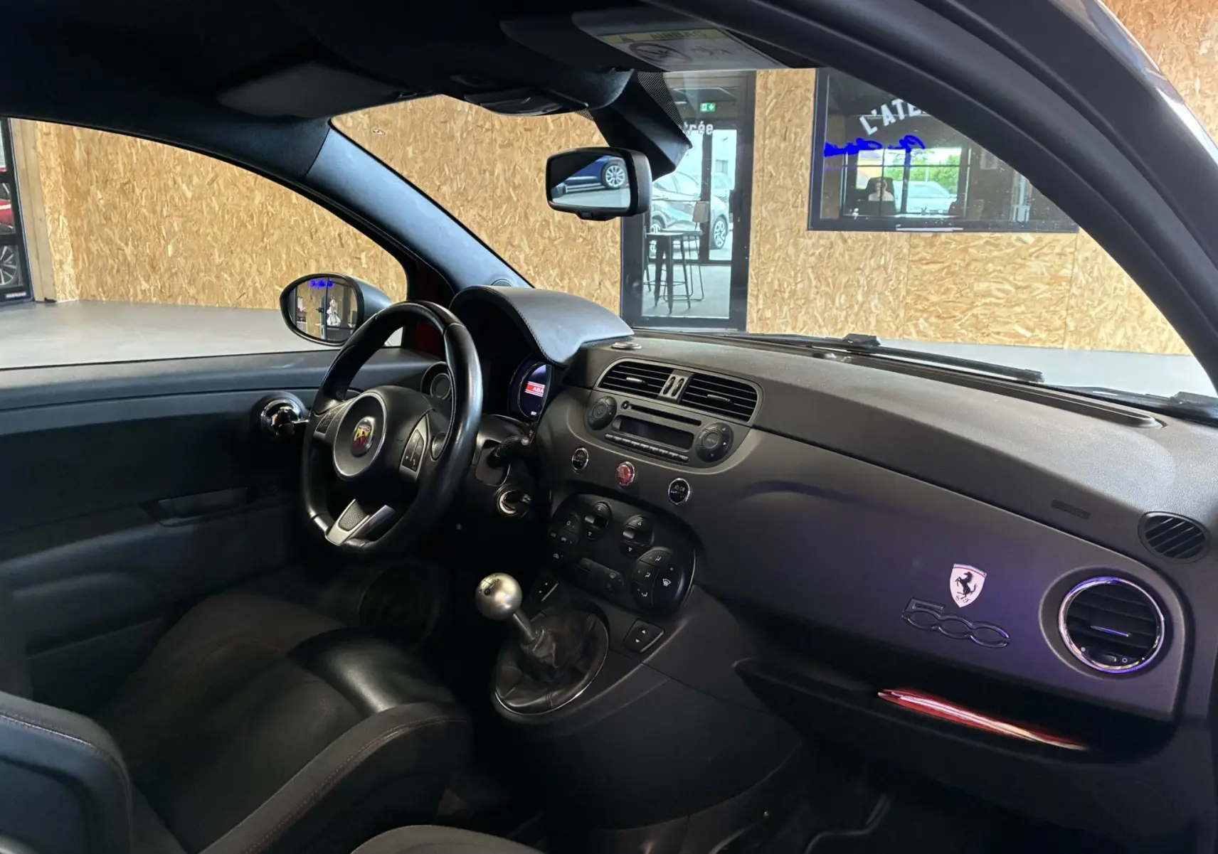Vue intérieure côté conducteur de l'Abarth 500 Competizione 2016, volant noir, levier de vitesse manuel et tableau de bord gris.