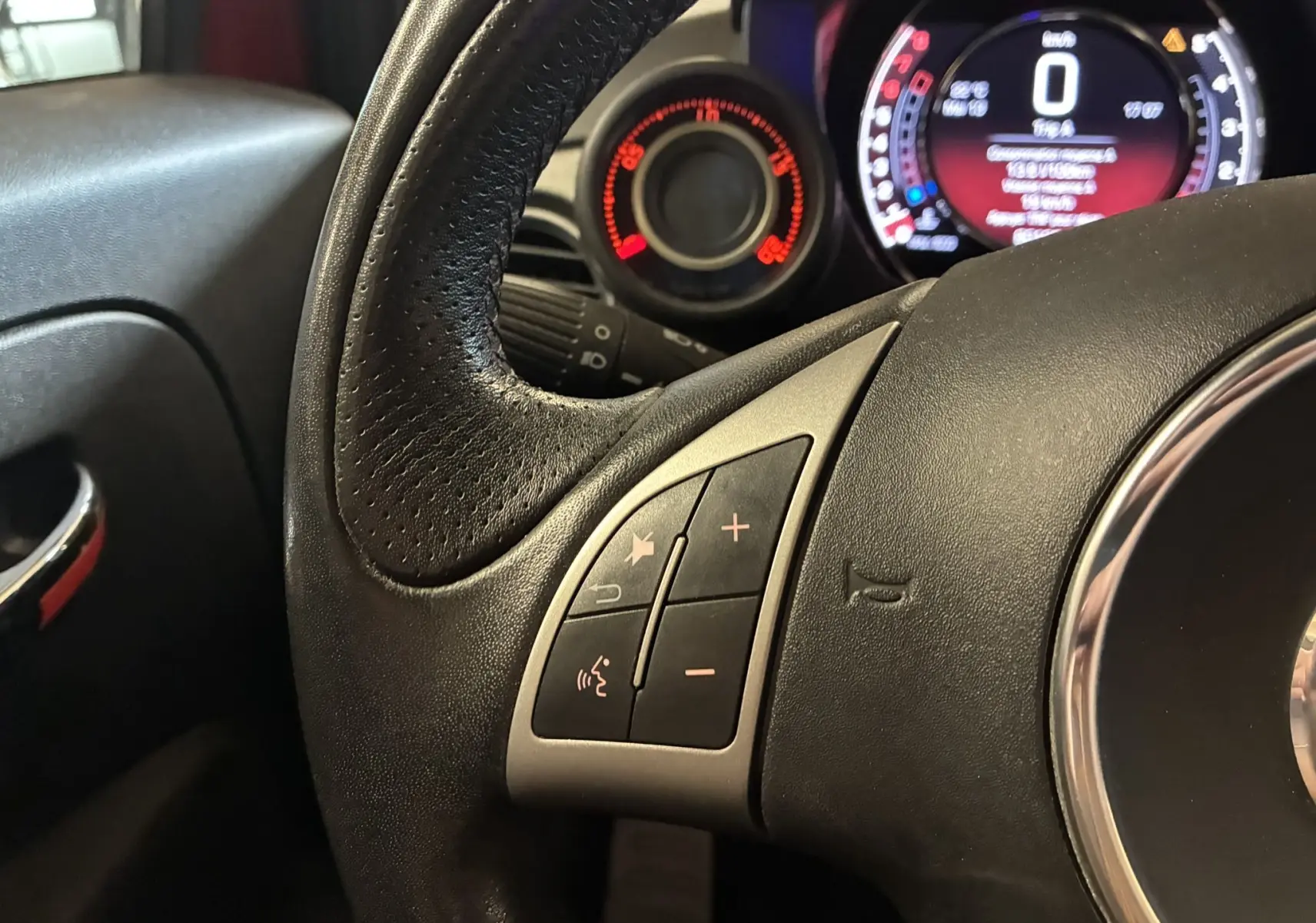 Gros plan sur le volant en cuir noir et le tableau de bord numérique rouge et gris de l'Abarth 500 Competizione 2016.