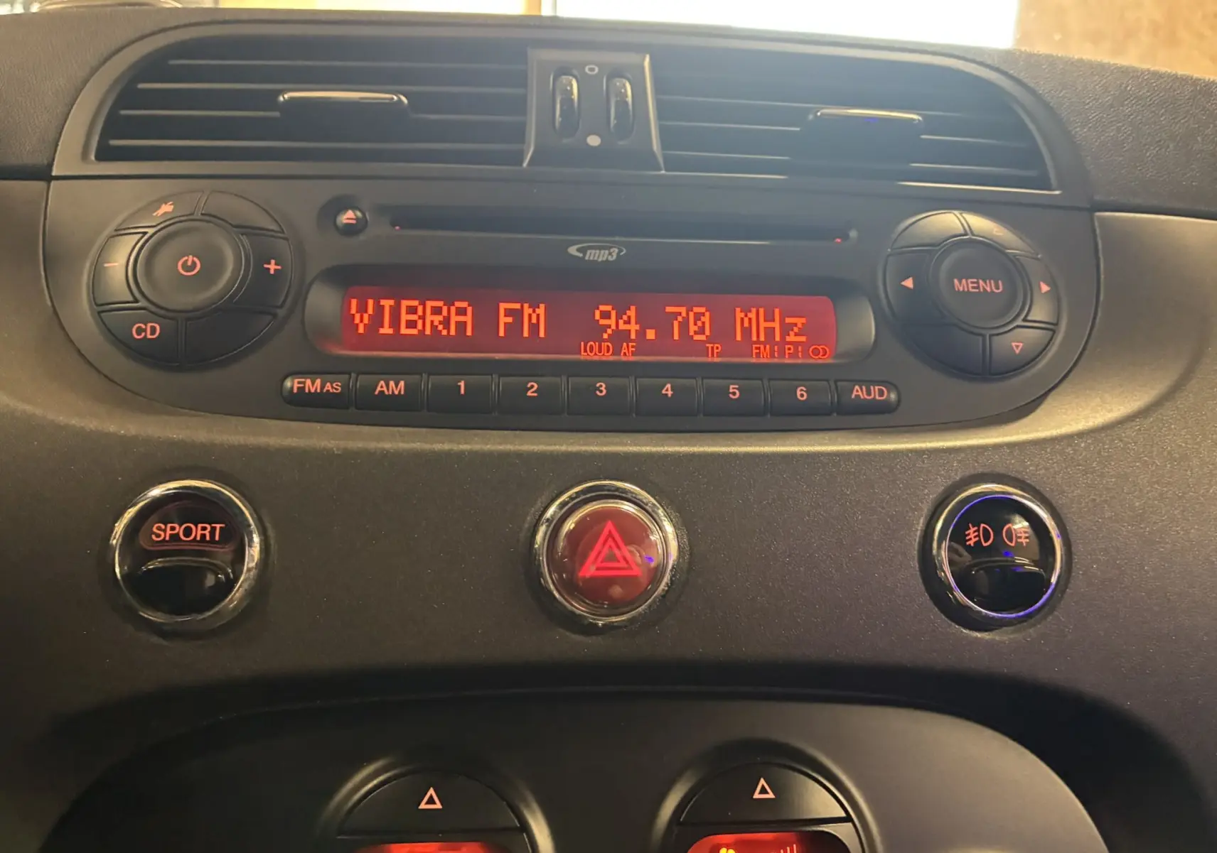 Vue rapprochée du tableau de bord de l'Abarth 500 Competizione 2016, avec radio allumée et boutons rouges SPORT et warning.