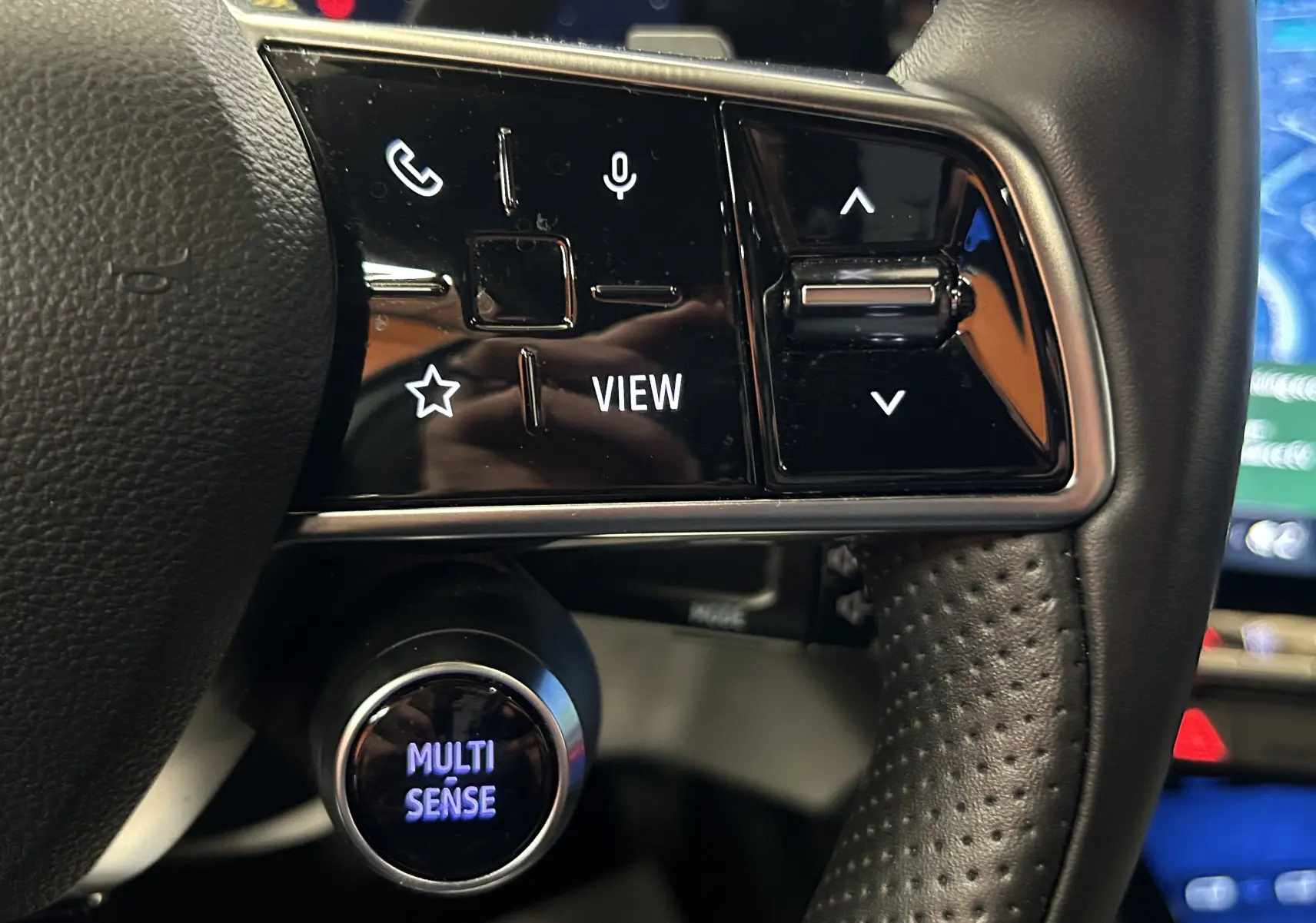 Gros plan sur les commandes noires du volant cuir perforé du Renault Austral blanc nacré, avec bouton Multi Sense éclairé.