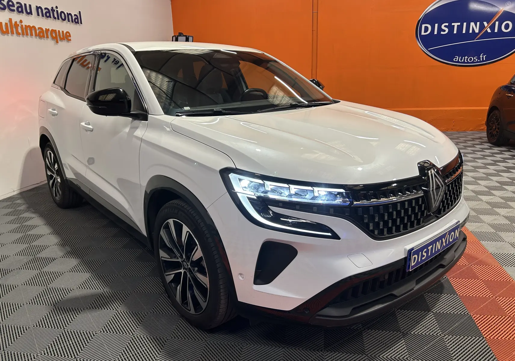Renault Austral blanc nacré en 3/4 avant droit, avec phares LED allumés et calandre noire distinctive.