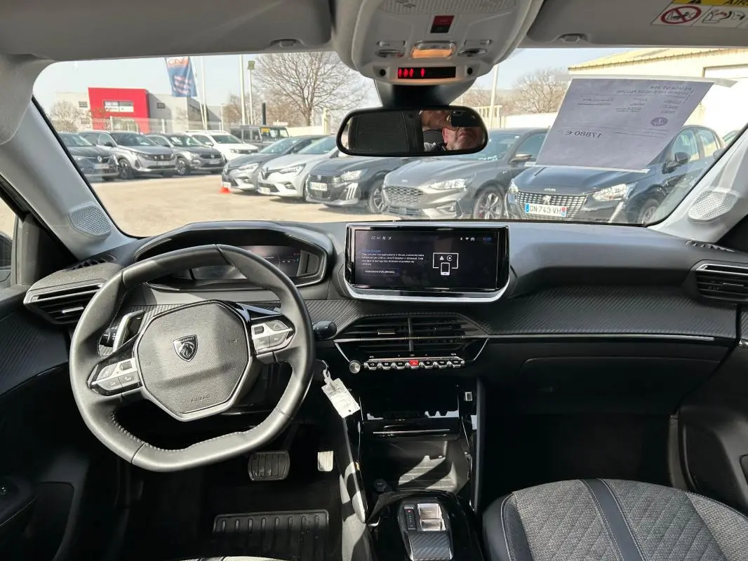 Vue intérieure avant de la Peugeot 208 Hybrid 110 e-DCS6 Allure 2024, tableau de bord moderne avec écran tactile et volant compact.