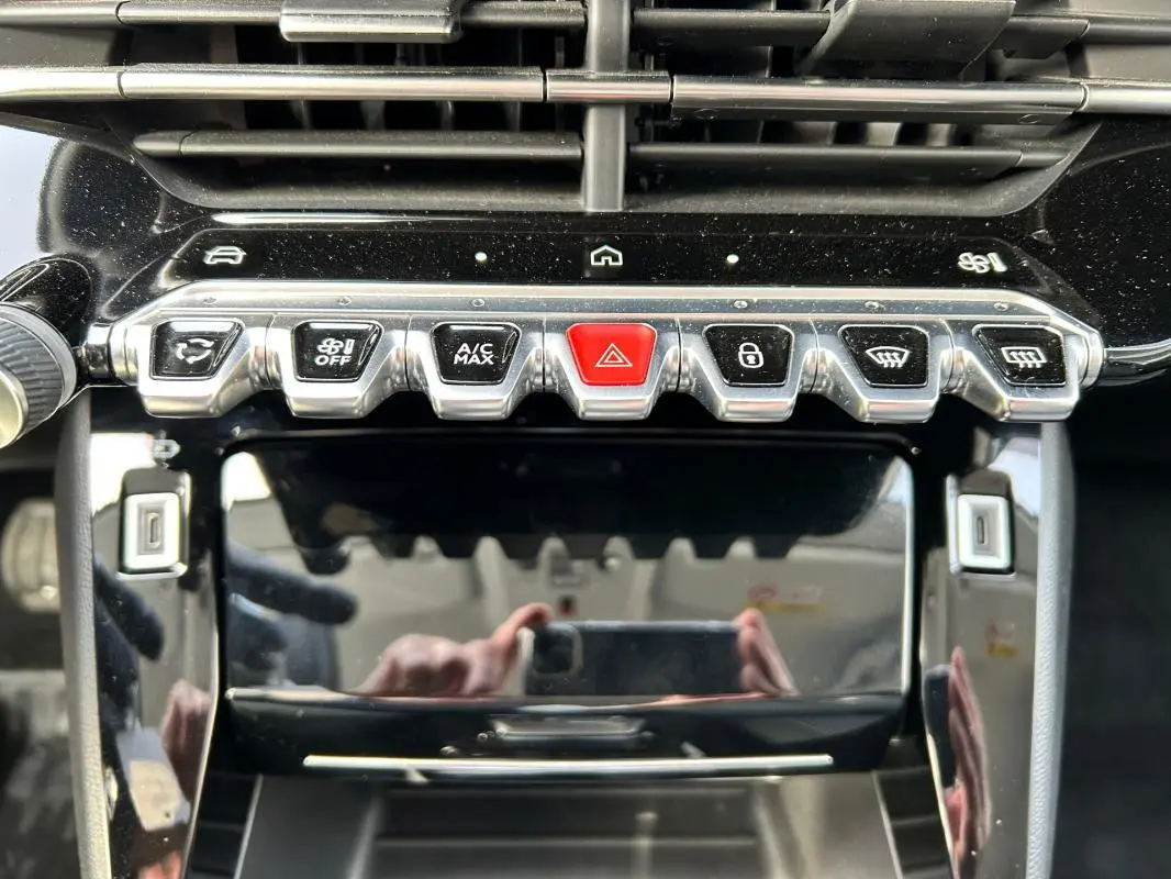 Détail de la console centrale du Peugeot 208 Hybrid 110 Allure 2024, avec boutons chromés et bouton rouge d’alerte.