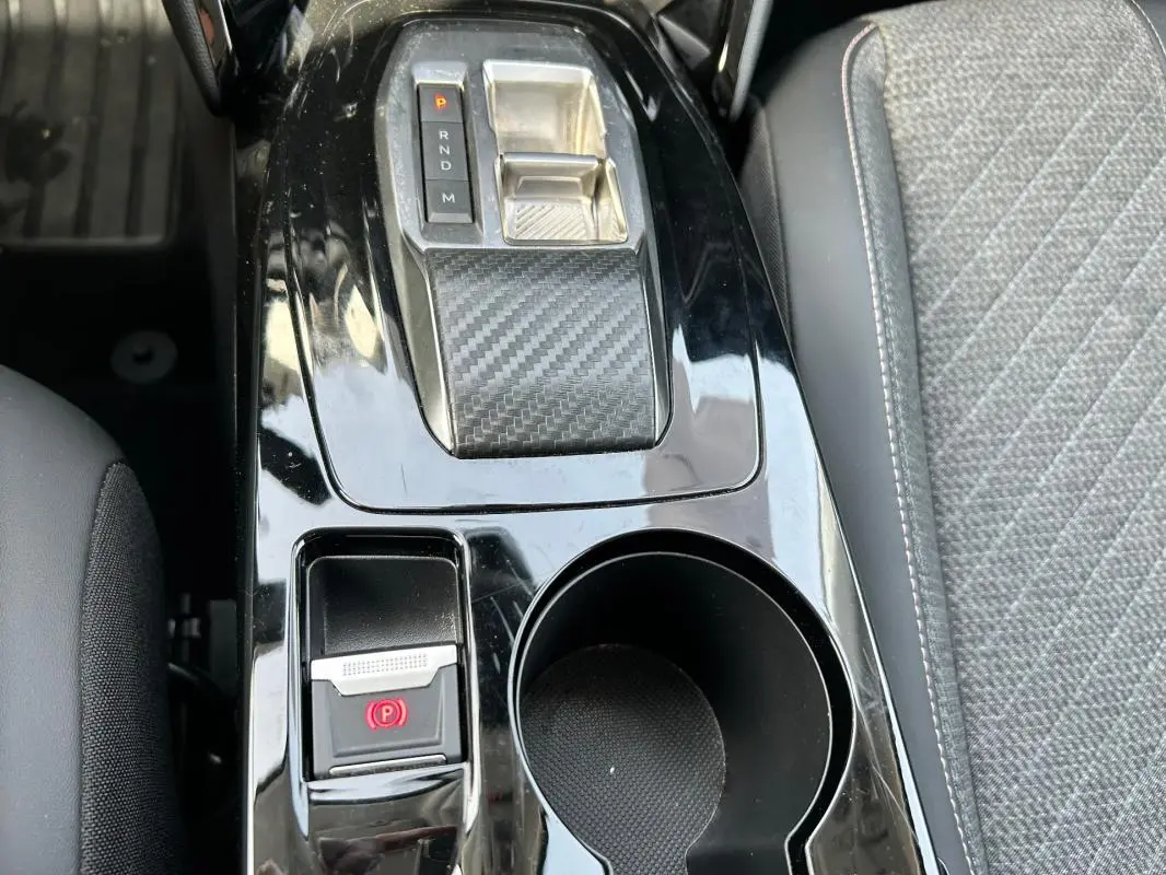 Vue rapprochée de la console centrale noire brillante avec levier de vitesse automatique et bouton de frein à main électrique sur Peugeot 208 gris.