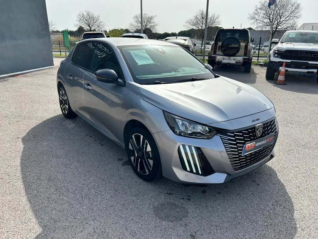Peugeot 208 Hybrid gris vue 3/4 avant droit, avec calandre distinctive et feux LED verticaux marquants.