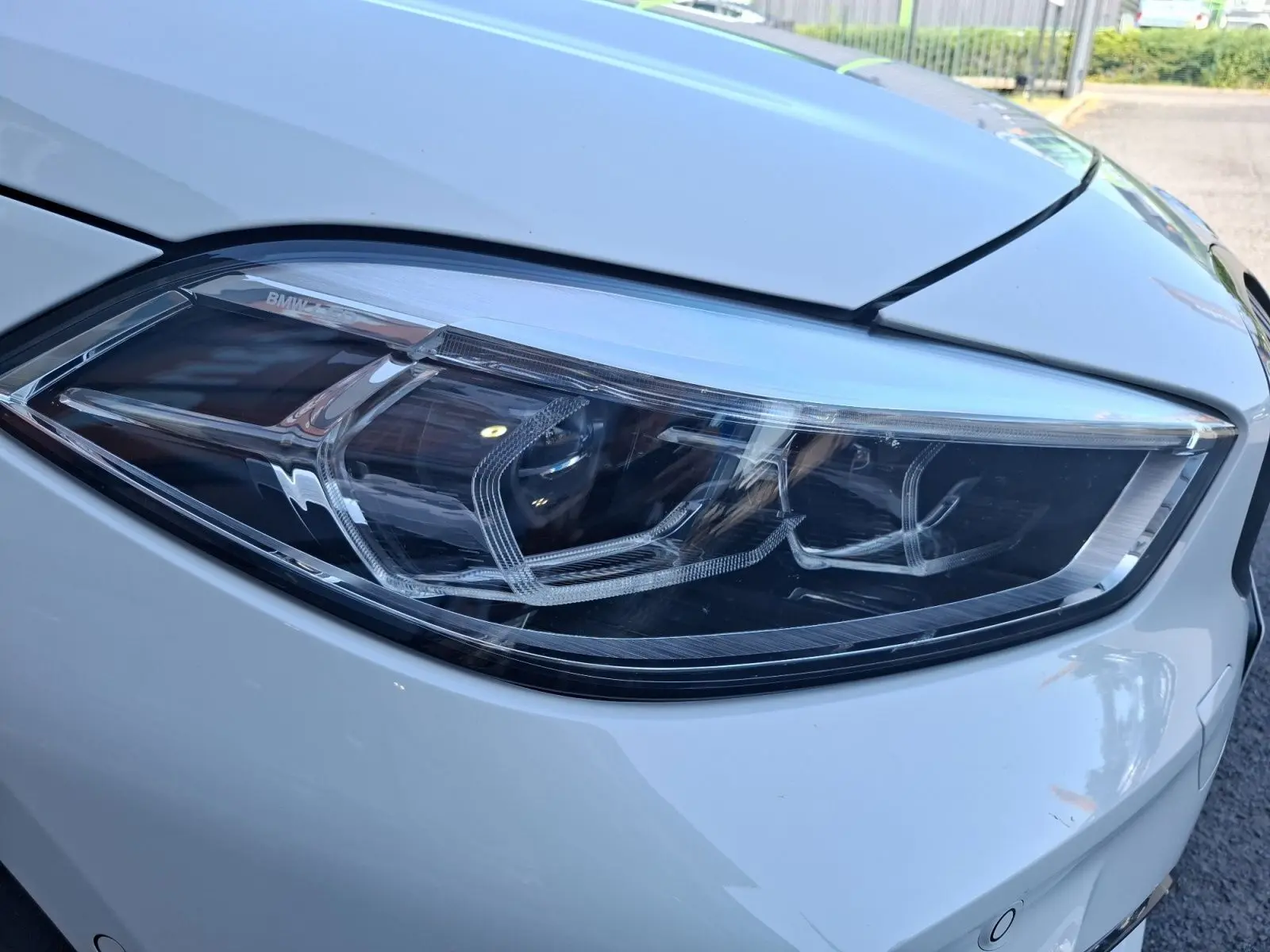 Gros plan sur le phare avant droit de la BMW Série 1 118D M Sport blanc, mettant en valeur ses détails LED modernes.