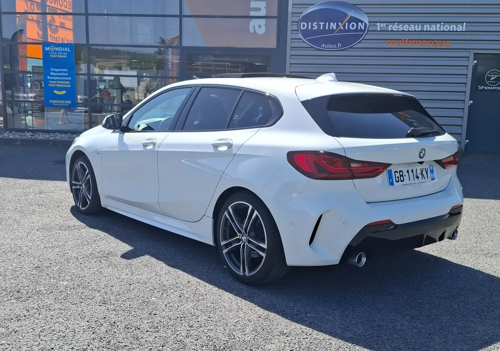 BMW Série 1 118D M Sport blanc vue 3/4 arrière droit, jantes alliage 18 pouces et vitres arrière surteintées.