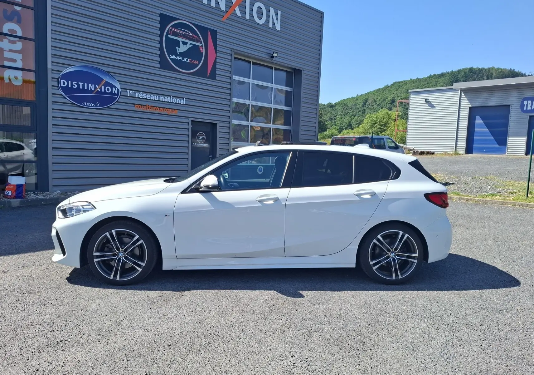 BMW Série 1 118D M Sport blanc vue de profil côté gauche, jantes alliage 18 pouces et vitres arrière surteintées.