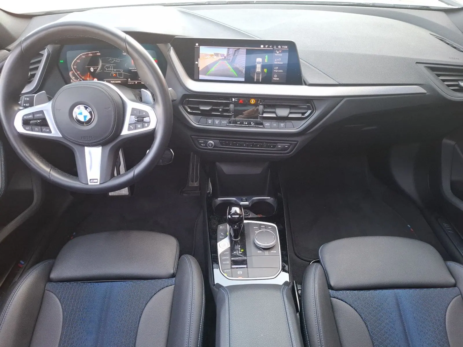 Vue intérieure avant de la BMW Série 1 118D M Sport blanche, avec volant multifonction, écran central et sellerie cuir/tissu.