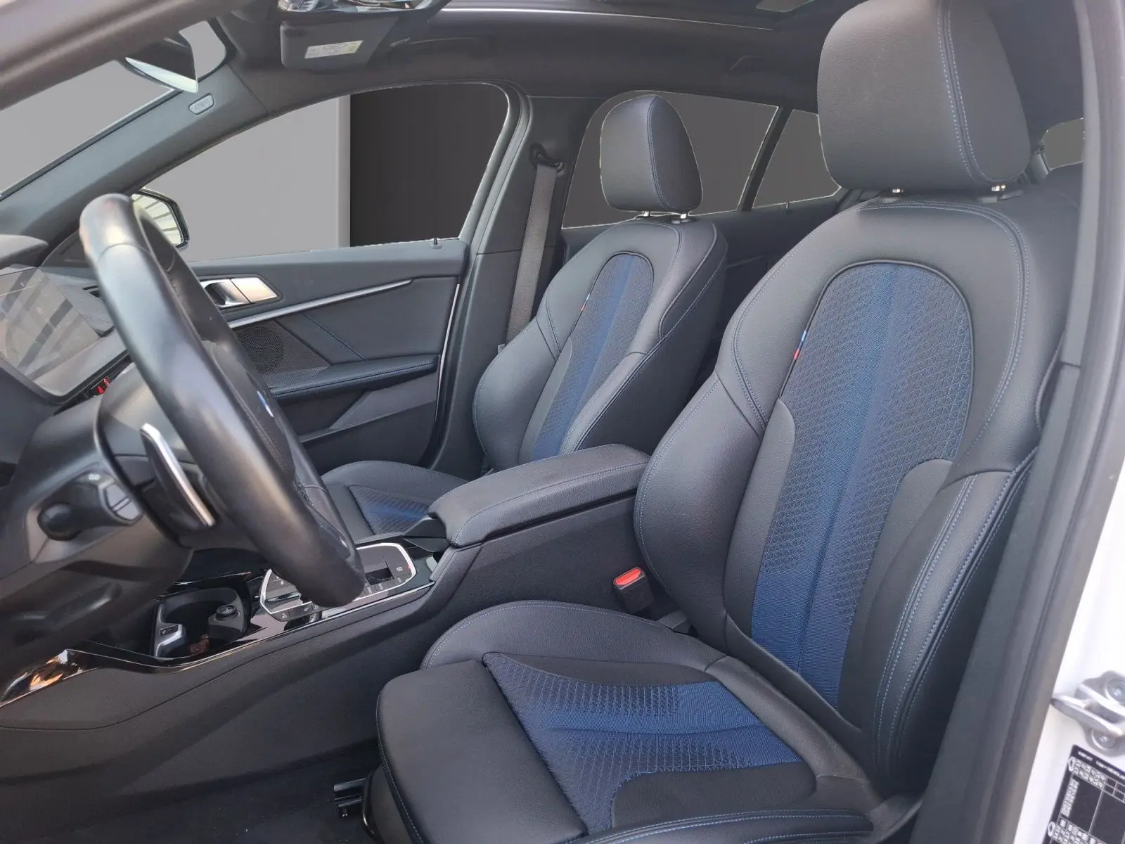 Vue intérieure côté conducteur de la BMW Série 1 118D M Sport blanc, sièges baquets cuir/tissu bleu et noir.