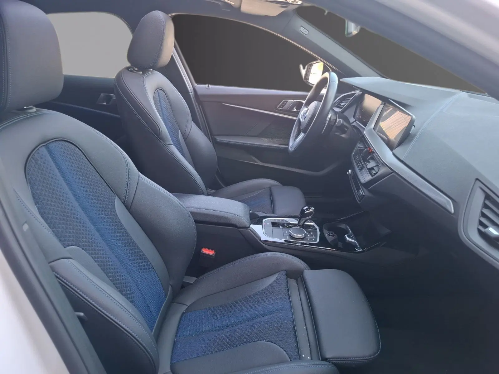 Vue intérieure côté conducteur de la BMW Série 1 118D M Sport avec sièges baquets cuir et tissu noirs et bleus.