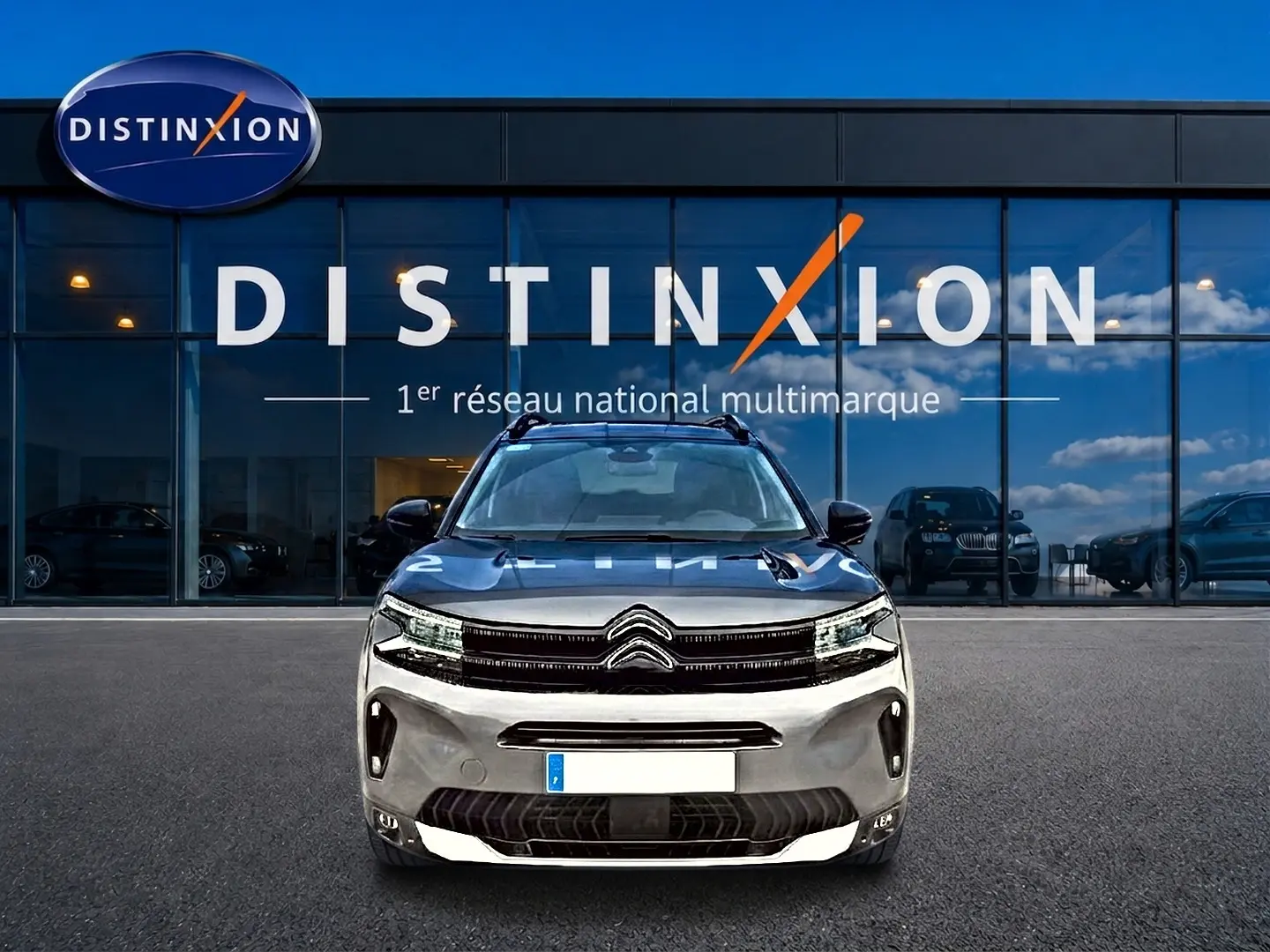 Citroën C5 Aircross gris vue de face, avec barres de toit et calandre distinctive, devant un showroom Distinxion.