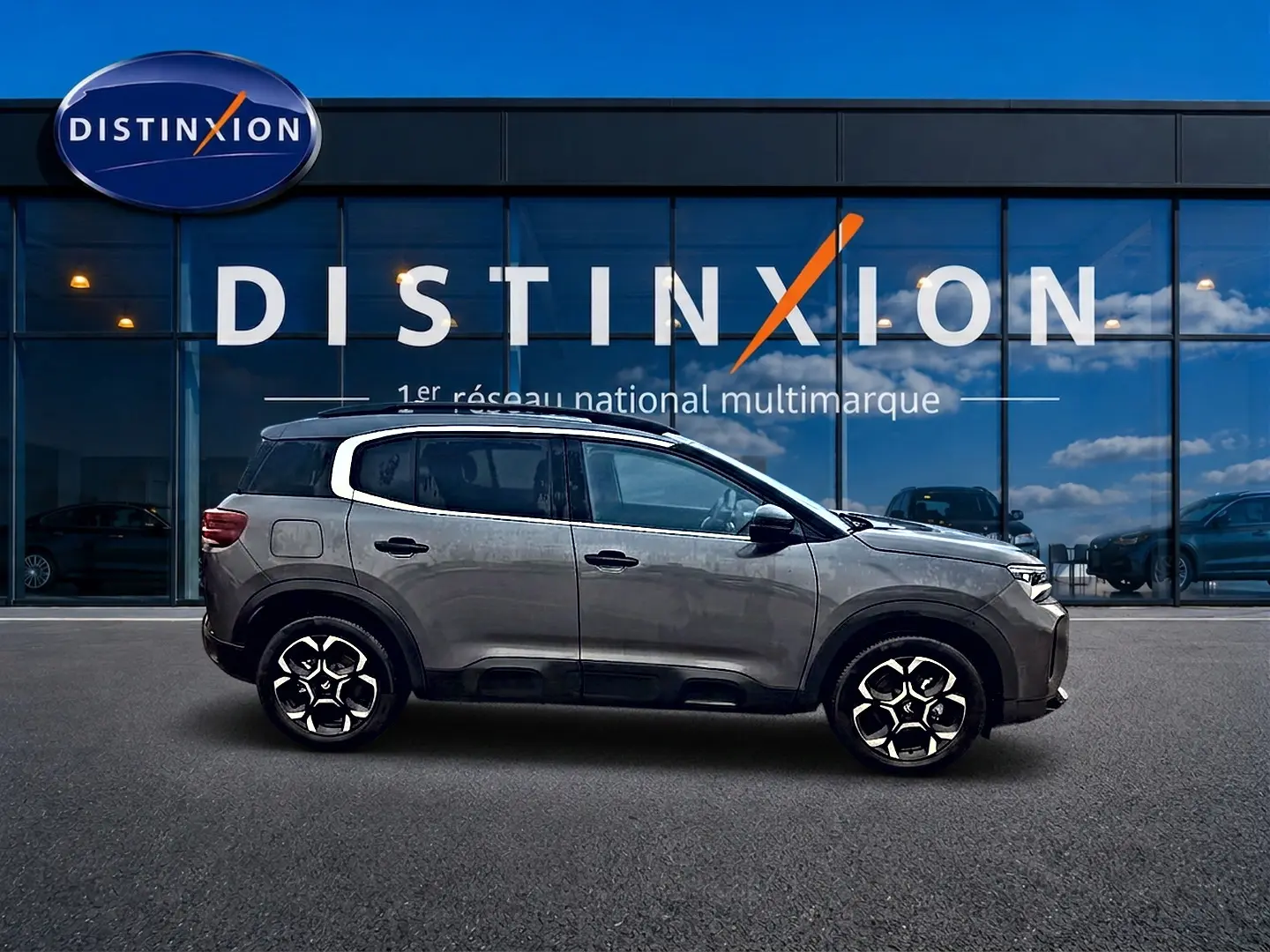 Profil côté gauche d'un Citroën C5 Aircross gris 2025 avec jantes alu et vitres arrière teintées devant un showroom Distinxion.