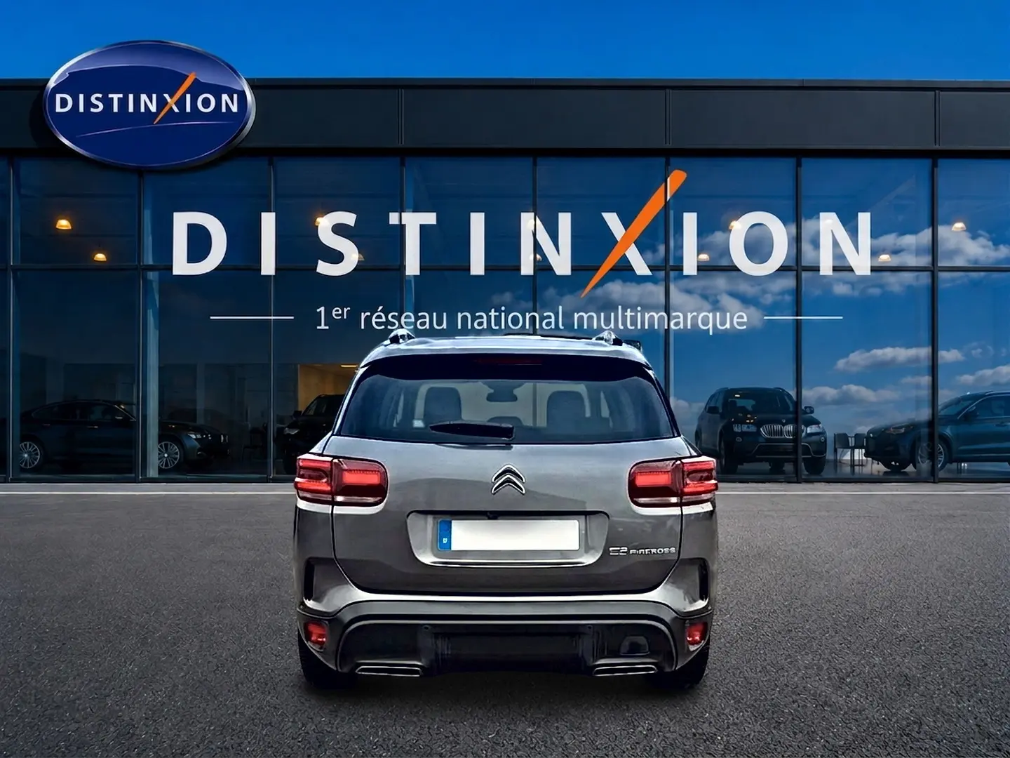 Vue arrière d'un Citroën C5 Aircross gris 2025 garé devant une vitrine avec logo Distinxion.