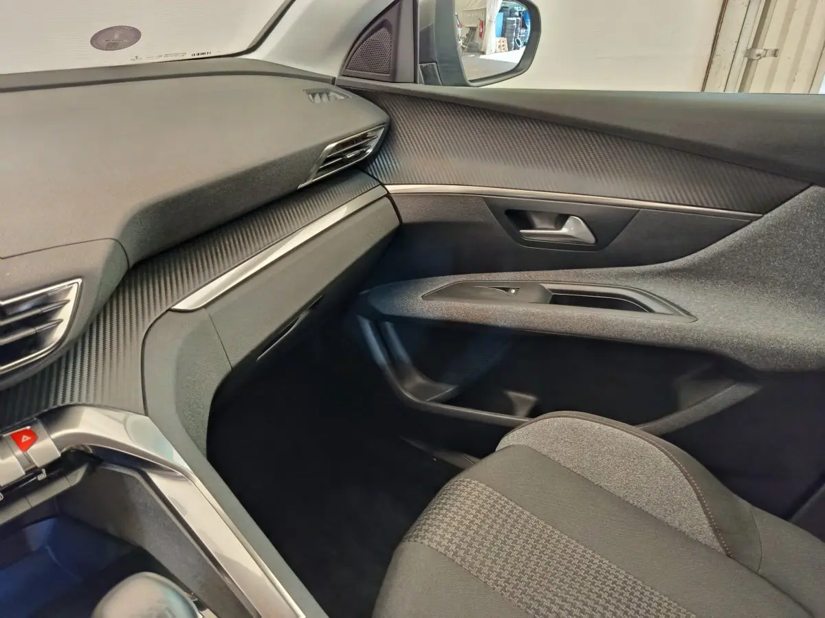 Intérieur côté passager du Peugeot 3008 gris foncé, avec tableau de bord texturé et siège tissu à motifs.