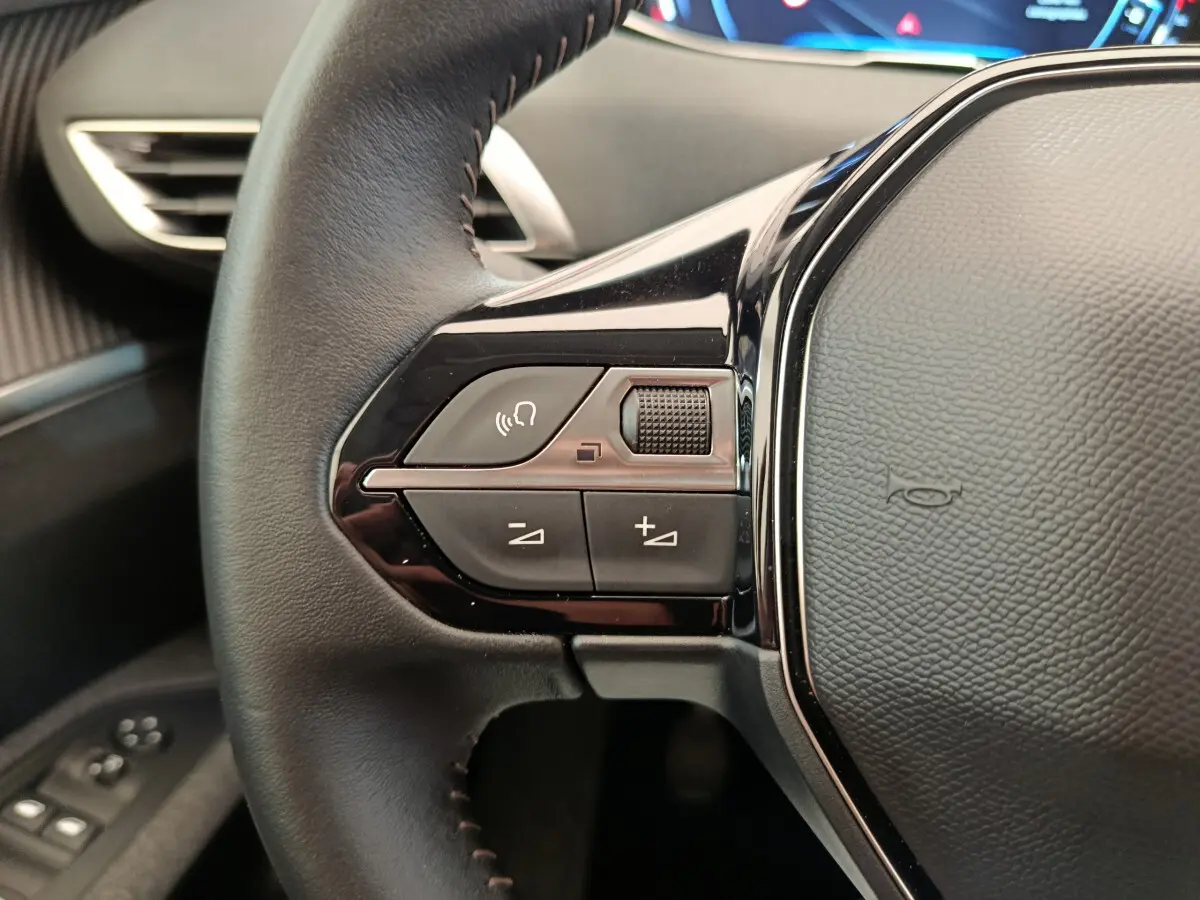 Gros plan sur le volant cuir noir du Peugeot 3008 2020, avec commandes audio et affichage numérique en arrière-plan.