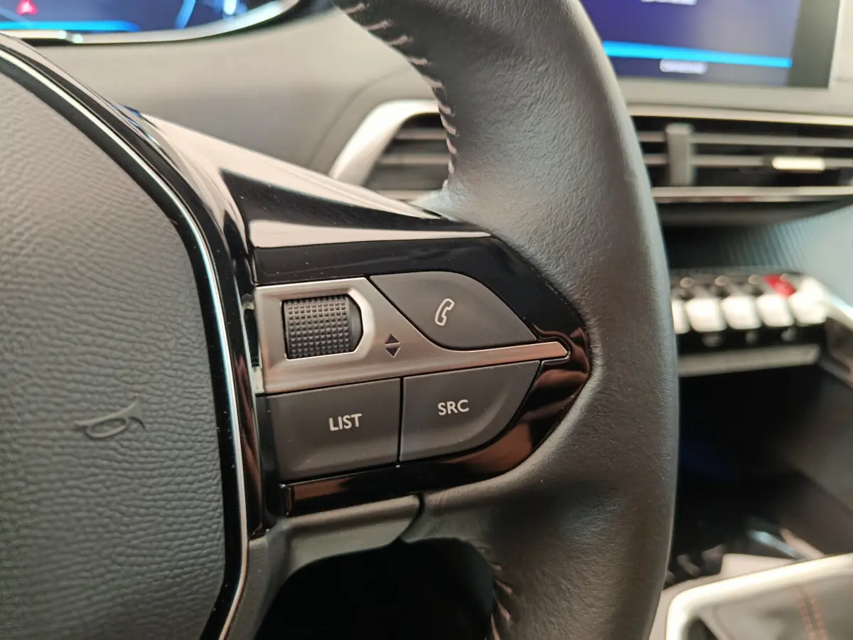 Gros plan sur les commandes gauche du volant cuir du Peugeot 3008 gris foncé, avec tableau de bord en arrière-plan.